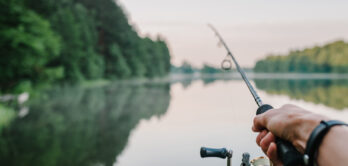 Fisherman with rod, spinning reel on the river bank. Sunrise. Fishing for pike, perch, carp. Fog against the backdrop of lake. background Misty morning. wild nature. The concept of a rural getaway.
