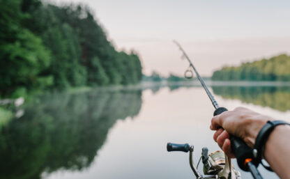 Fisherman with rod, spinning reel on the river bank. Sunrise. Fishing for pike, perch, carp. Fog against the backdrop of lake. background Misty morning. wild nature. The concept of a rural getaway.
